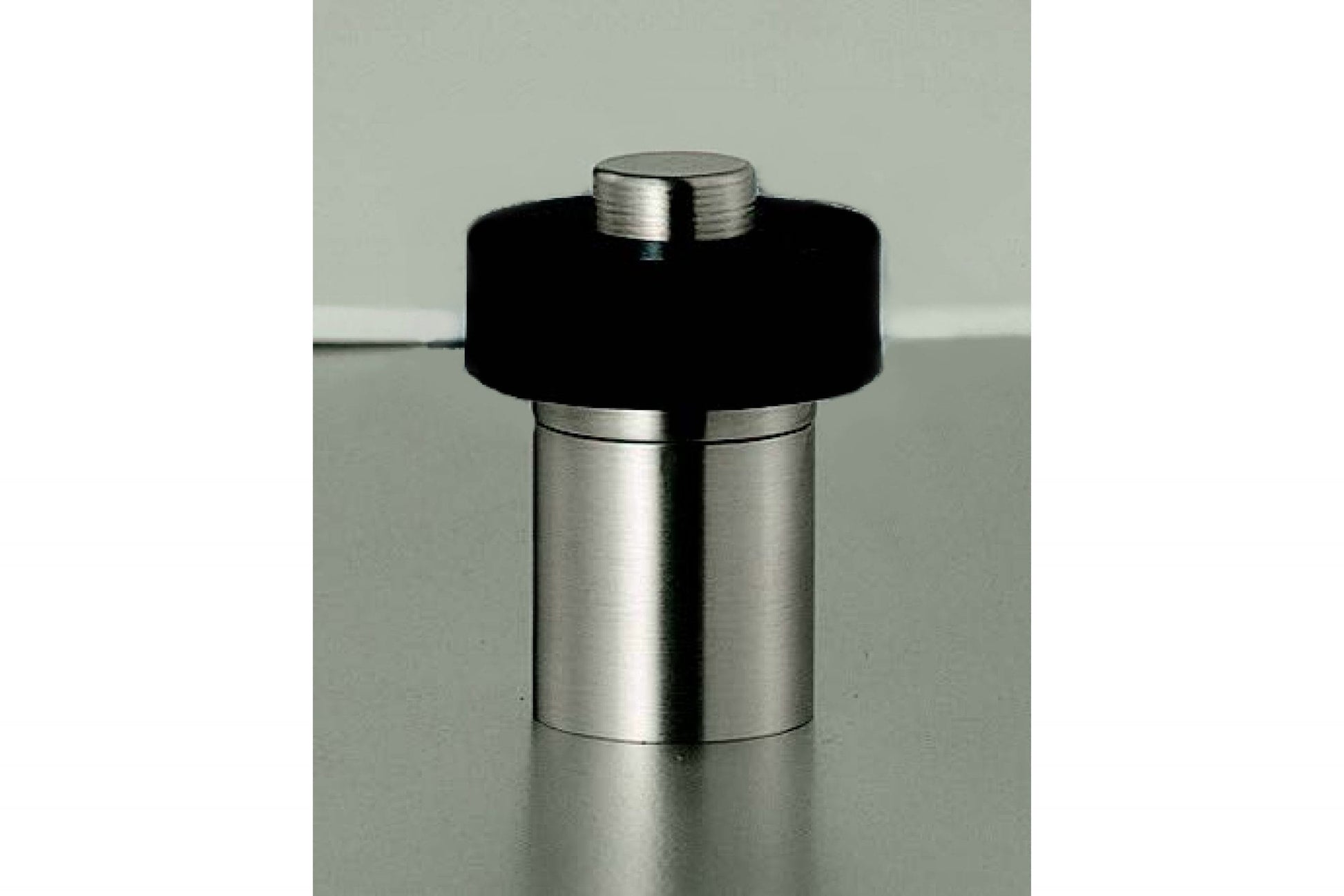 Metallic cylindrical object with black top on a reflective surface